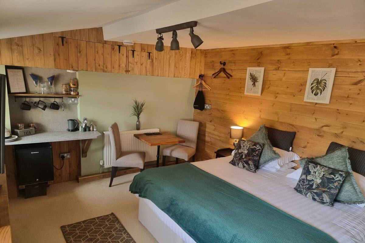 Habitación pequeña con cama, un escritorio y una silla. Hay un radiador debajo del escritorio y una lámpara en la mesita de noche.