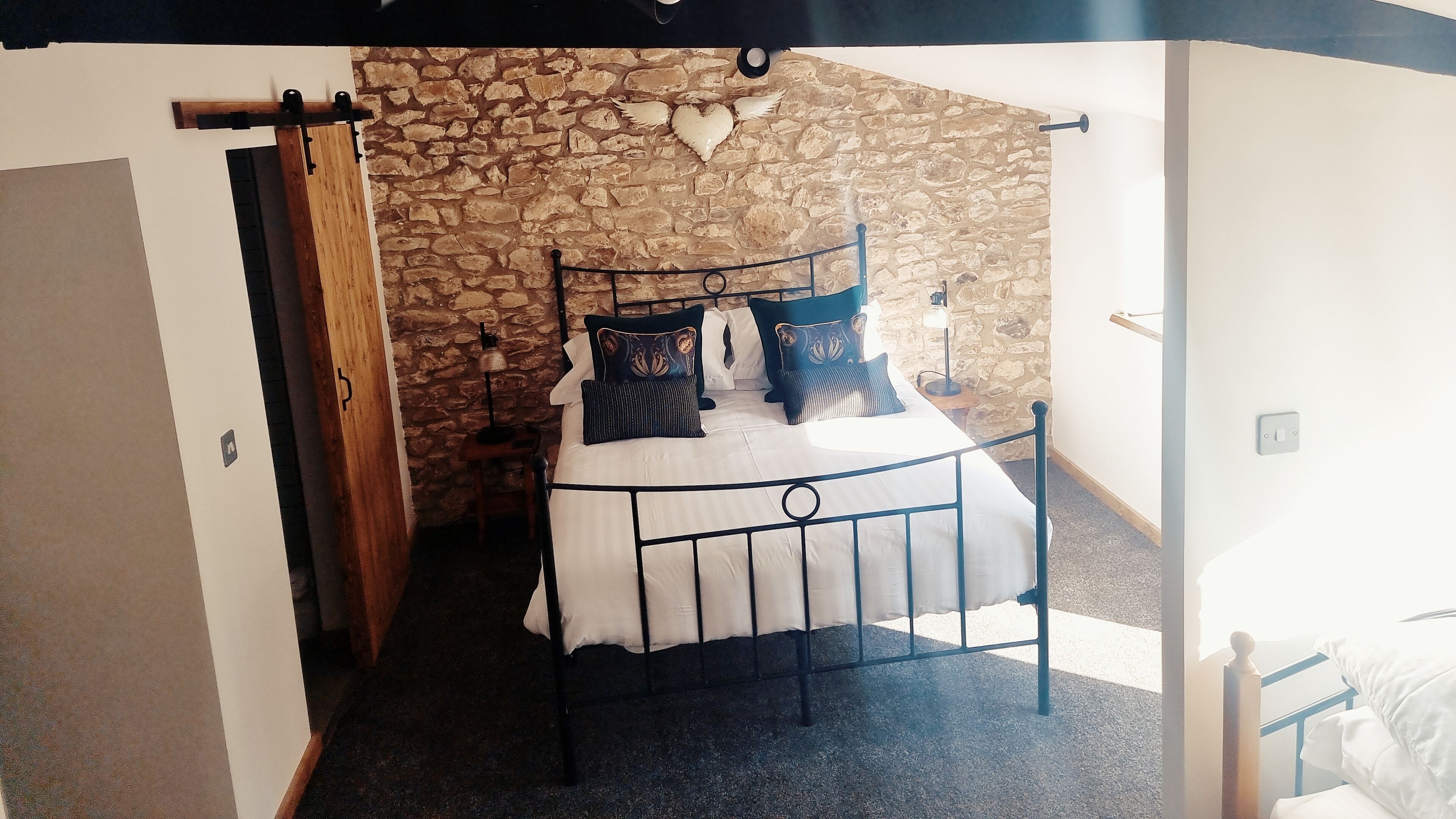 Une chambre avec un mur en pierre, un lit avec un cadre en métal et une table de chevet avec une lampe.