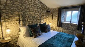 A bedroom with a stone wall, a bed with a white and teal bedspread, and a nightstand with a lamp.