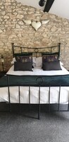 Una cama con estructura metálica, ropa de cama blanca y almohadas decorativas frente a una pared de piedra.