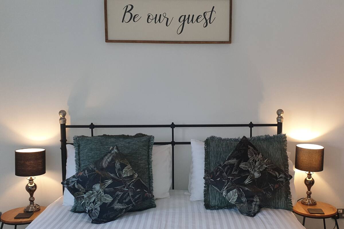 Una cama bien hecha con dos almohadas, dos lámparas de noche y un cartel enmarcado encima.
