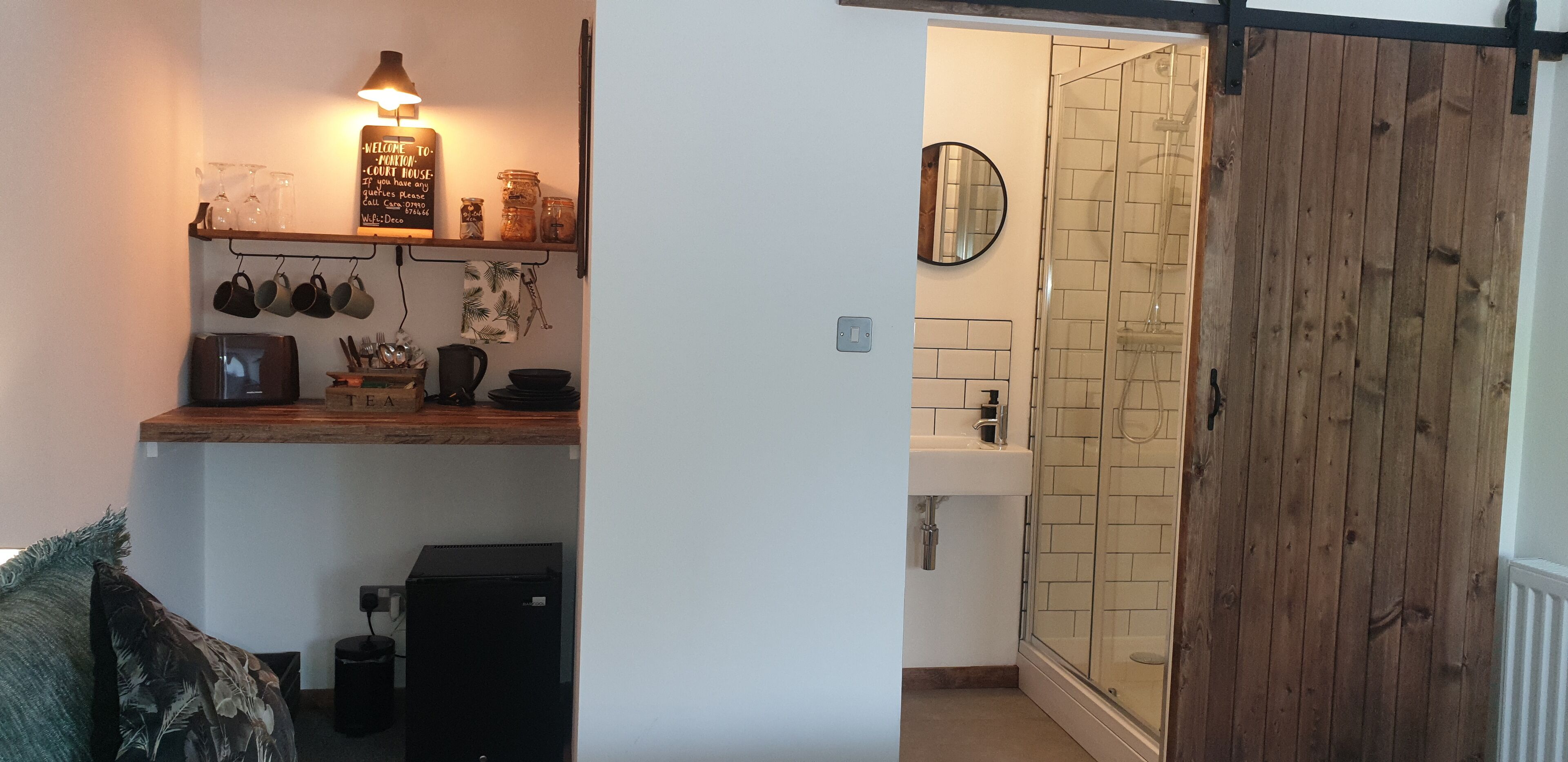 A kitchen with a wooden shelf holding mugs, a kettle, and a sign.