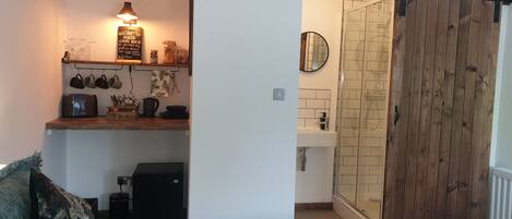 A kitchen with a wooden shelf holding mugs, a kettle, and a sign.