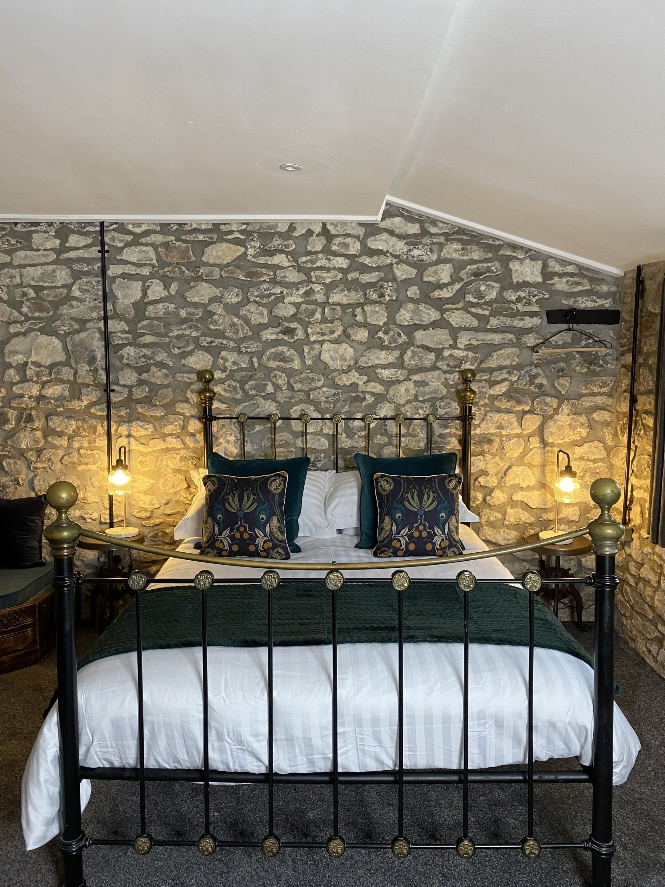 Una cama con un cabecero de pared de piedra, una lámpara colgante y una mesita de noche con lámpara.