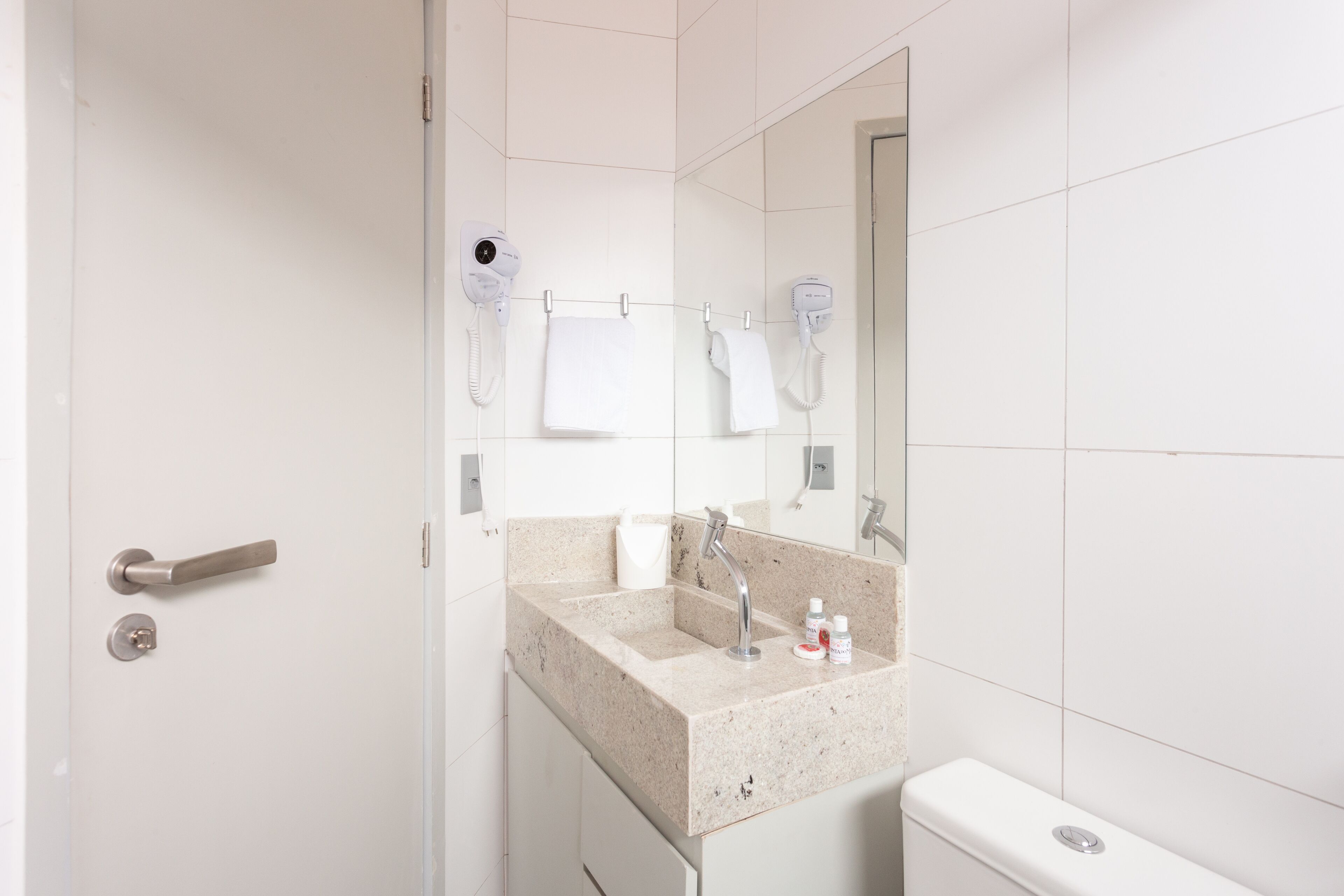 Een moderne badkamer met een wastafel, spiegel en twee haardrogerapparaten bevestigd aan de muur.