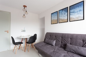 A modern living room with a grey sofa, black chairs, a white dining table, and three framed pictures on the wall.