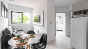 Uma zona de refeições moderna com uma mesa branca, cadeiras pretas e um frigorífico branco.