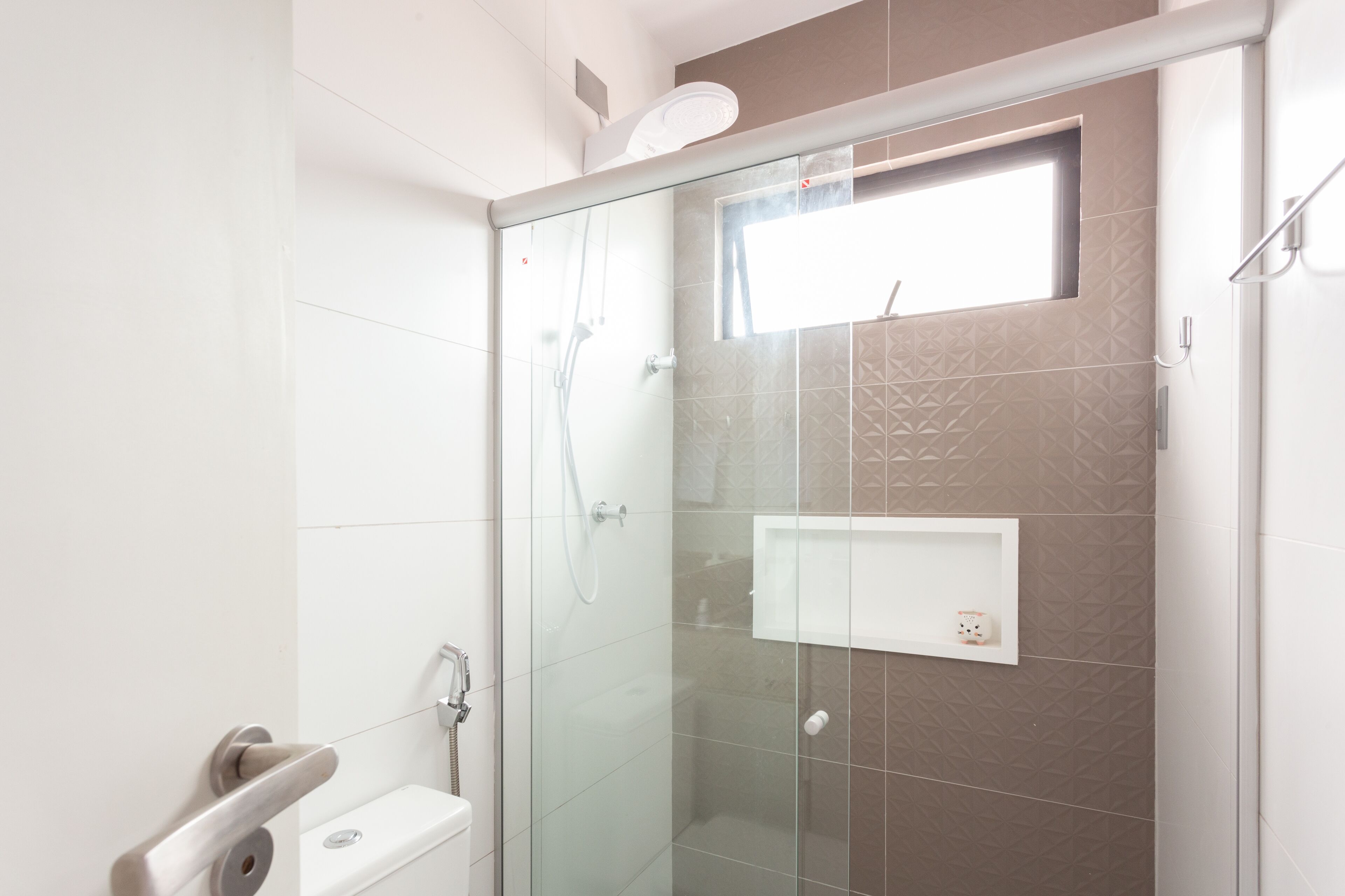 A modern bathroom with a glass shower enclosure, a small window, and a white sink.