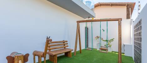 A patio with a wooden swing set, a bench, and a small table.