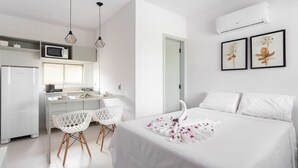 Quarto de hotel com cama, escrivaninha, duas cadeiras, ar condicionado e quadros na parede.