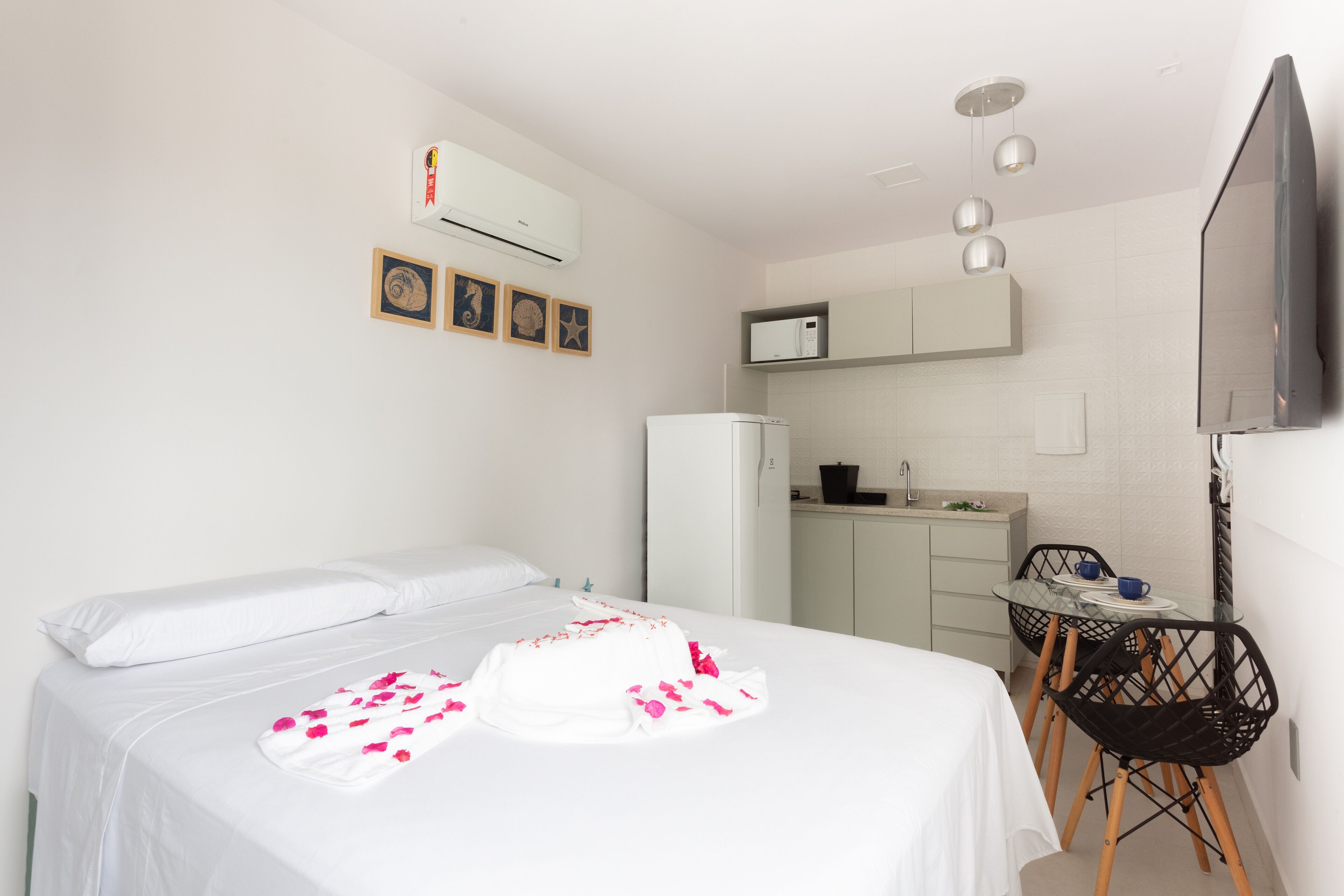 A hotel room with a bed, a small kitchenette, a TV, and a desk with chairs.