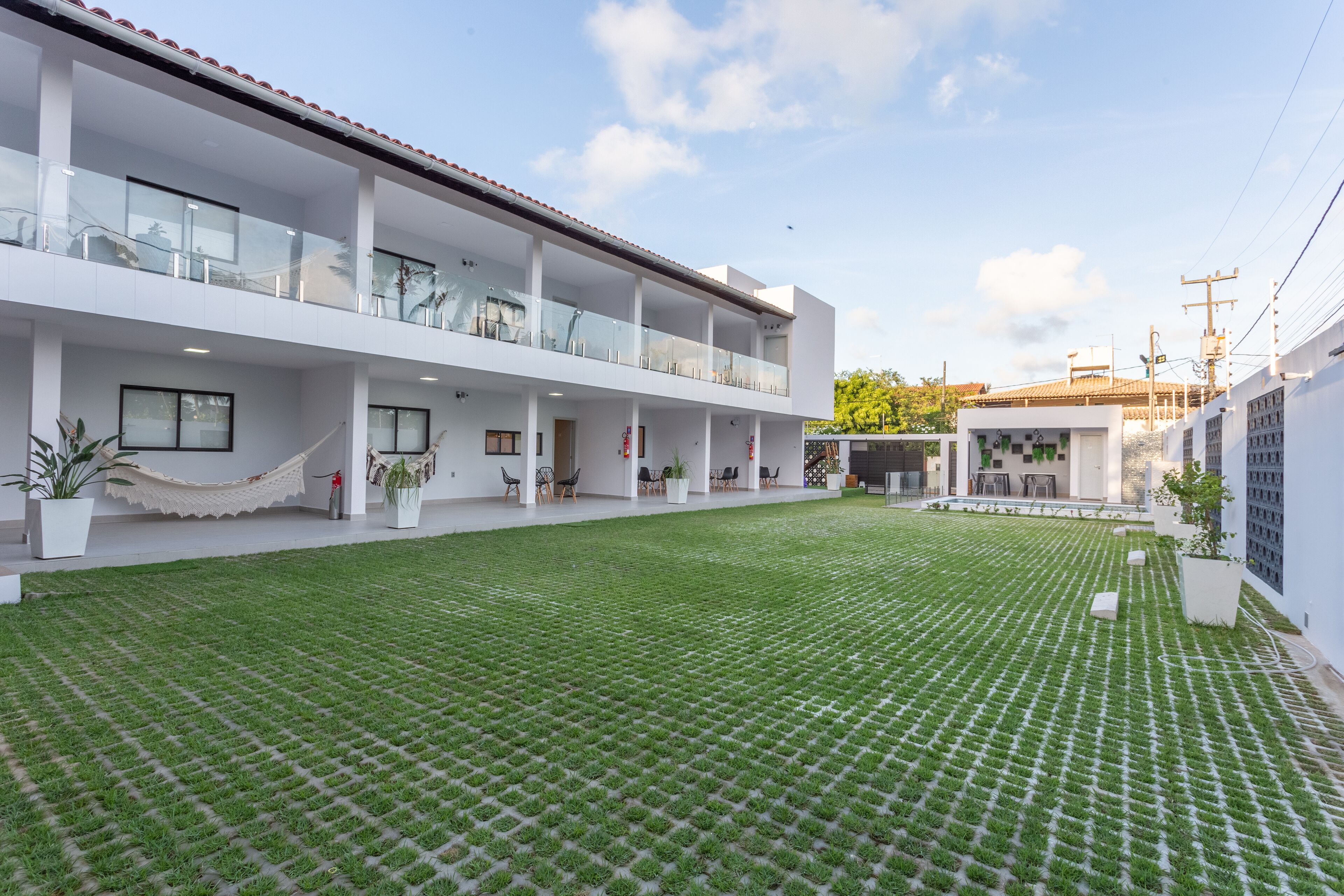 Um edifício moderno com um pátio amplo, com gramado padronizado, área de estar externa e vasos de plantas.