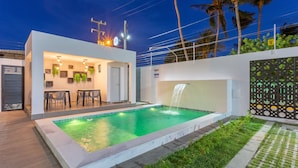 Uma área de piscina moderna ao ar livre, com espaço para refeições e um elemento aquático.