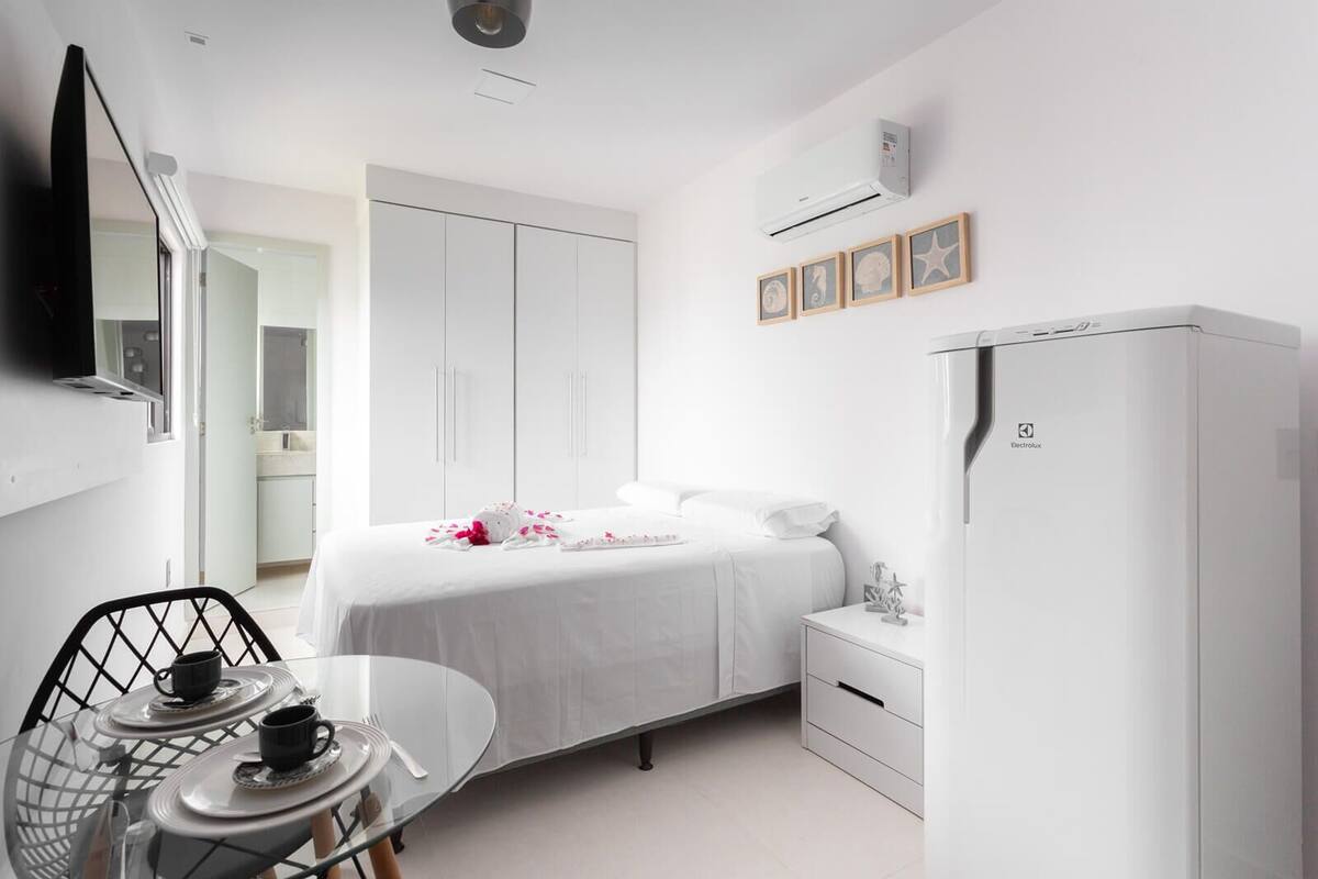 A modern hotel room with a bed, a desk with a chair, a wardrobe, and an air conditioning unit.