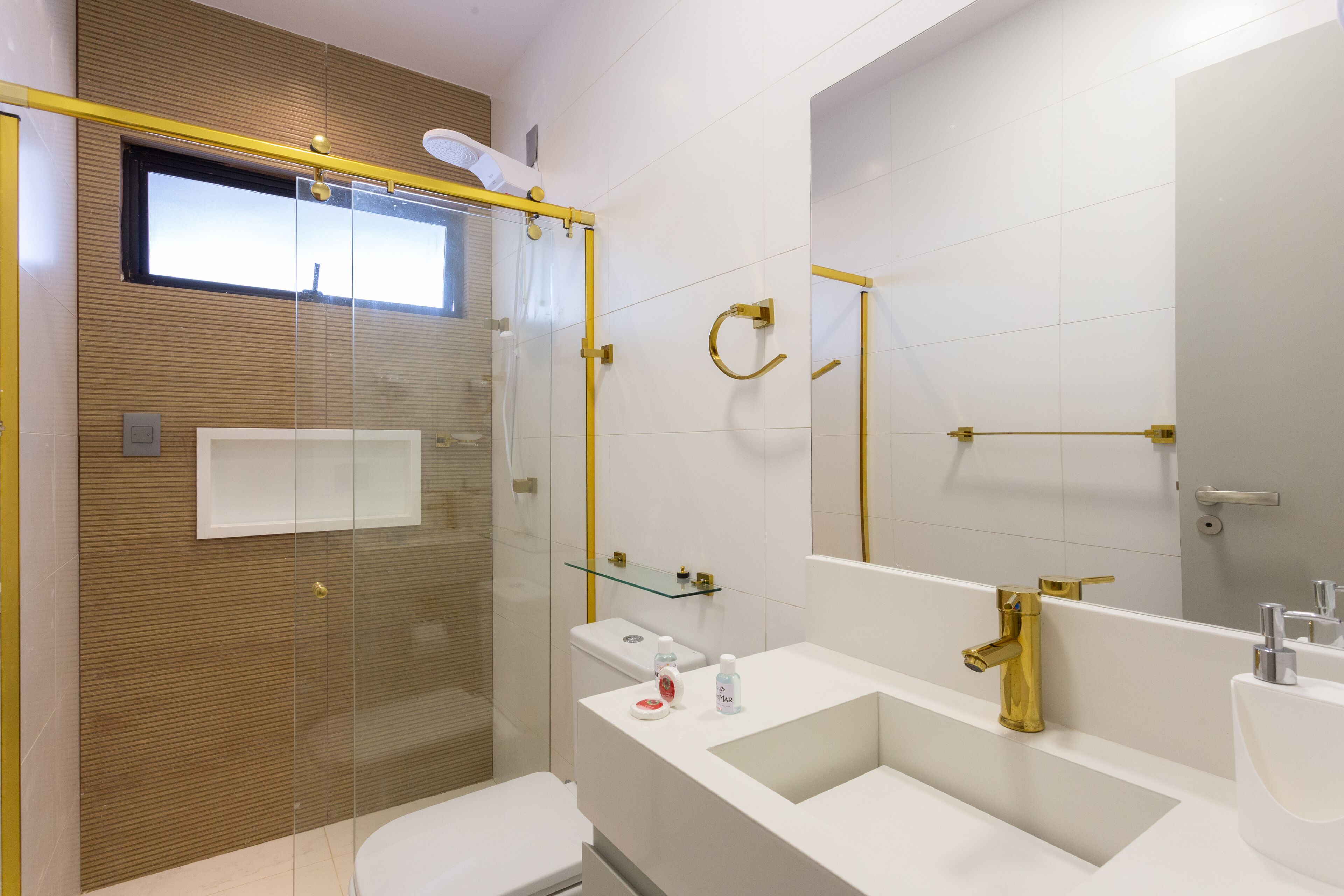 A modern bathroom with a glass shower enclosure, a white sink with gold fixtures, and a large mirror.