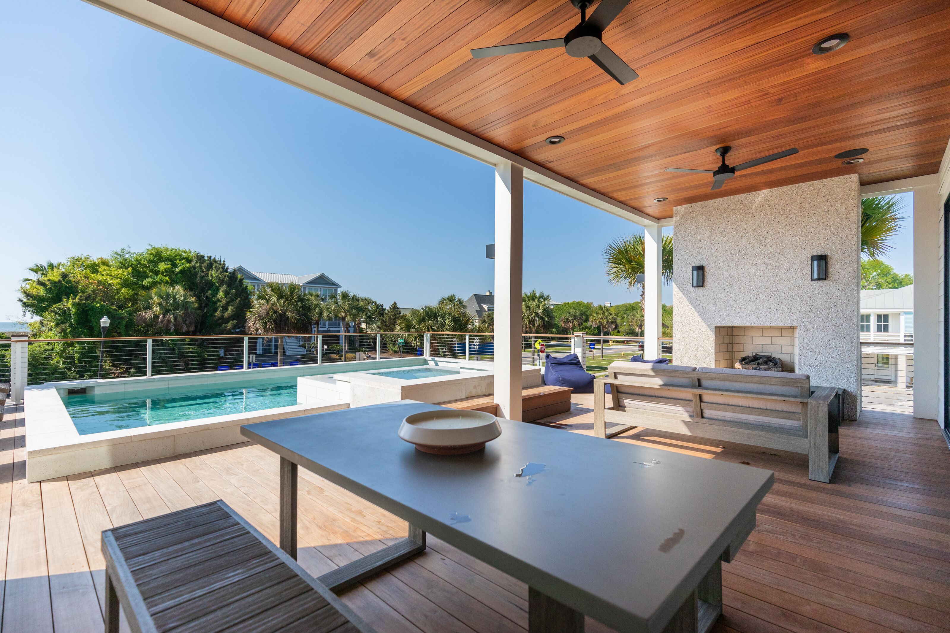 A modern outdoor deck with a pool, wooden furniture, and a stone wall.
