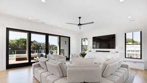 Un salon moderne avec un canapé d’angle, un téléviseur à écran plat et un ventilateur de plafond.