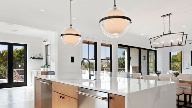 Une cuisine moderne dotée d’un grand îlot central, de luminaires suspendus et offrant une vue sur l’extérieur.