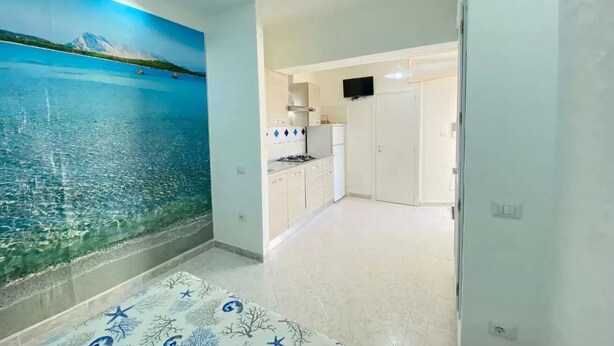 Una habitación con un amplio mural de una montaña y un lago, una cocina con armarios blancos y un televisor de pantalla plana montado sobre la encimera.