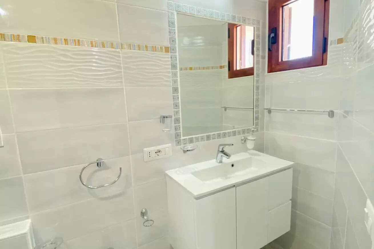 Un bagno con piastrelle bianche, un lavandino bianco, uno specchio e un porta asciugamani.