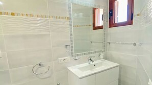 Un baño con azulejos blancos, un lavabo blanco, un espejo y un perchero para toallas.