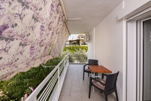 A balcony with a floral awning, a table, two chairs, and a view of neighboring buildings.