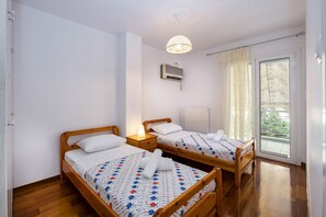A room with two wooden beds, a ceiling light, an air conditioning unit, and a window with curtains.