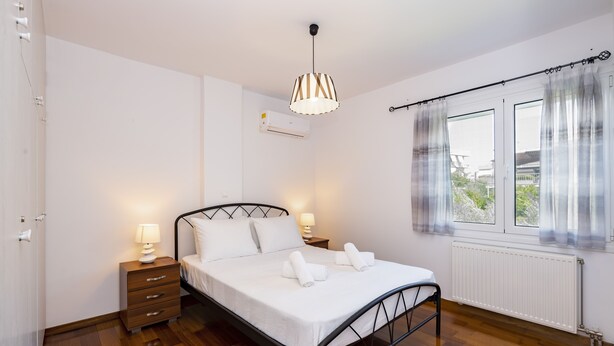 A bedroom with a bed, bedside tables, a hanging lamp, and a window with curtains. - Beautiful flat in superb location (Glyfada)
