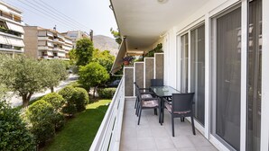 A balcony with a table and chairs, overlooking a well-maintained garden and a street with cars. - Beautiful flat in superb location (Glyfada)