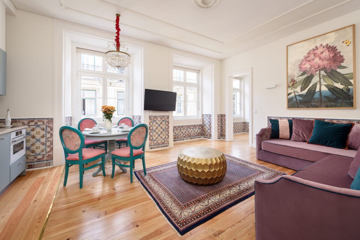 Un salon spacieux doté d’un plancher en bois, d’un canapé violet, d’un pouf rond et d’un coin repas avec une table et des chaises.