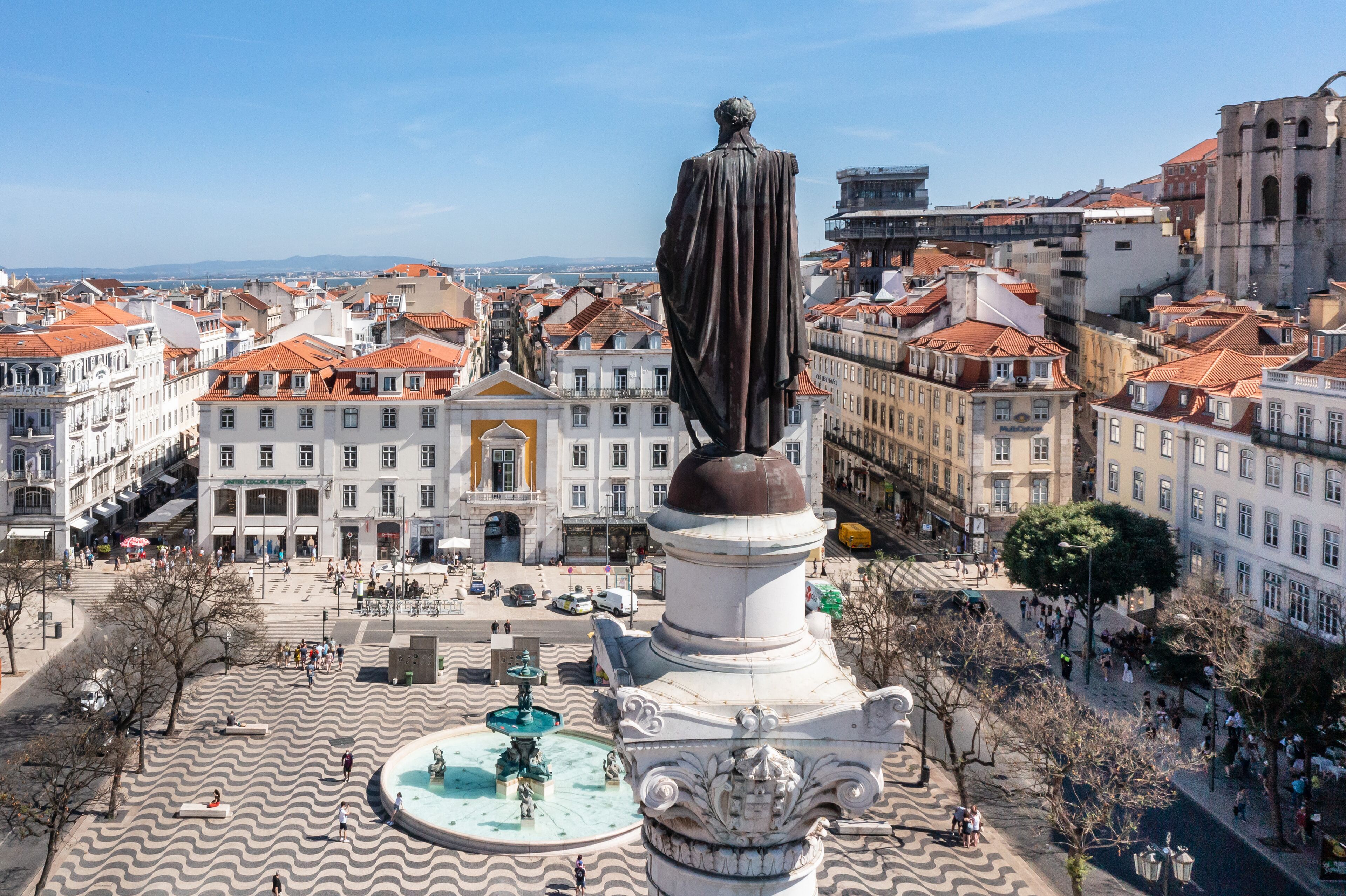 A plaza with a statue, fountain, and historic buildings.