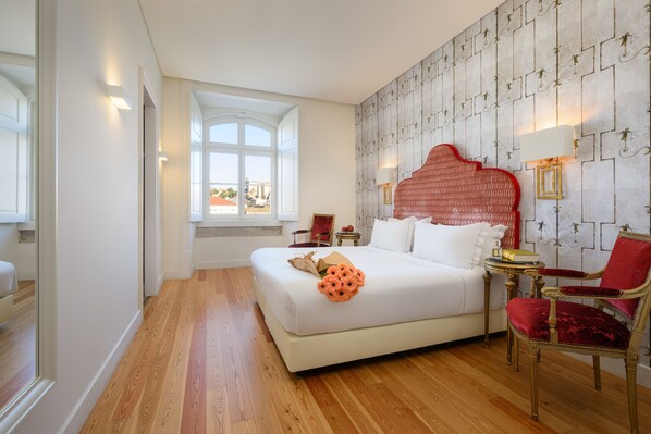 A bedroom with a large bed, a red upholstered chair, and a view of the outdoors through a window. - Residentas Arco do Bandeira (Lisbon)