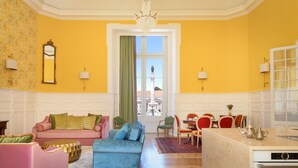 Une pièce lumineuse aux murs jaune vif, avec un canapé, un pouf et un coin repas.