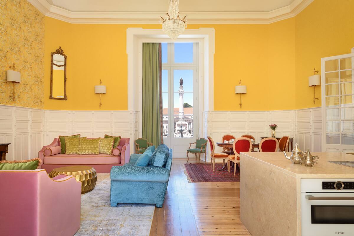 Une pièce lumineuse aux murs jaune vif, avec un canapé, un pouf et un coin repas.