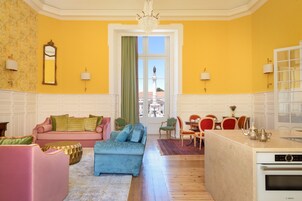 A bright yellow room with a sofa, ottoman, and dining area.