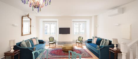 Un salón amplio con un sofá azul, una mesa de comedor con sillas, una araña y un espejo grande en la pared.