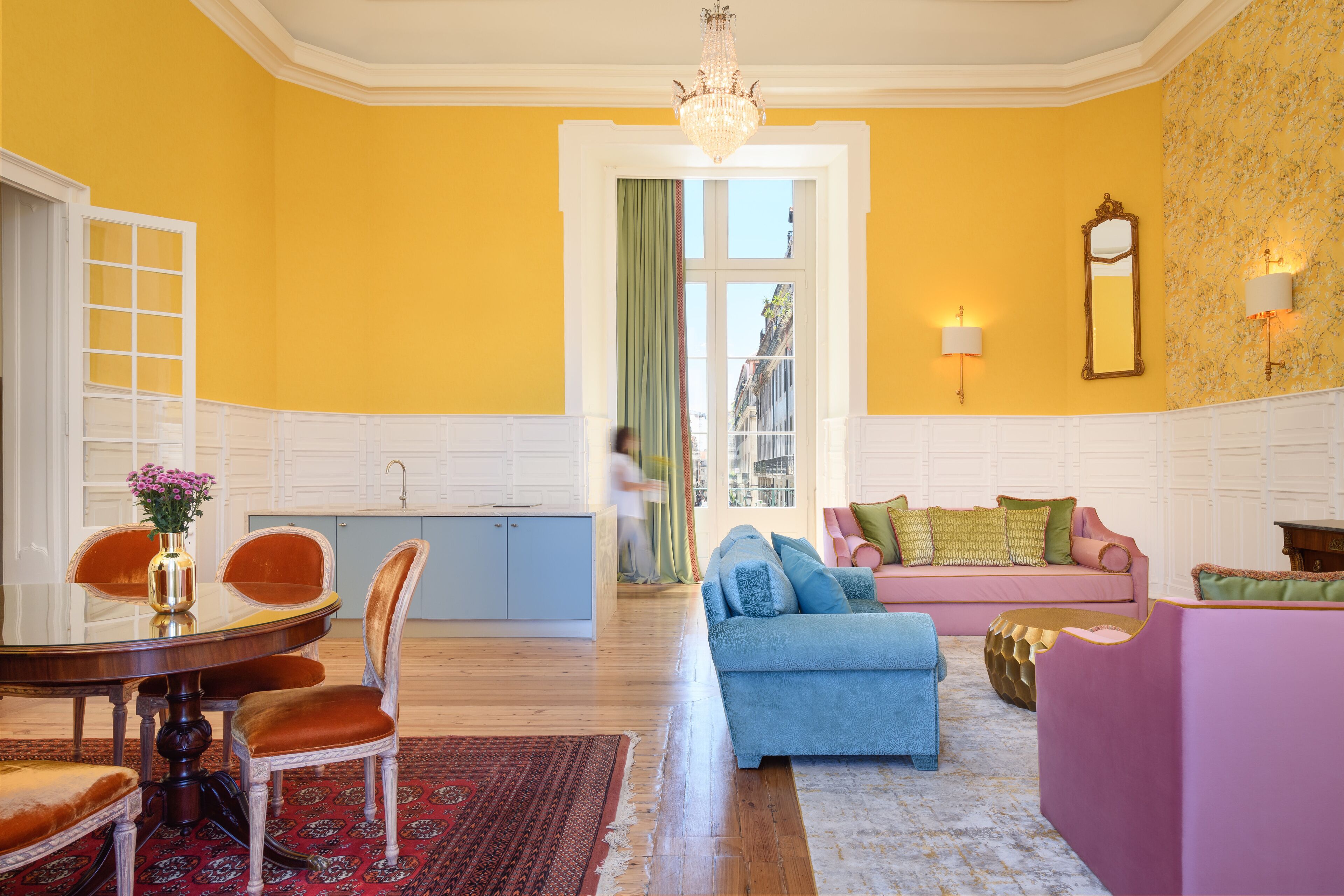 A room with a dining table, chairs, a sofa, and a patterned rug.