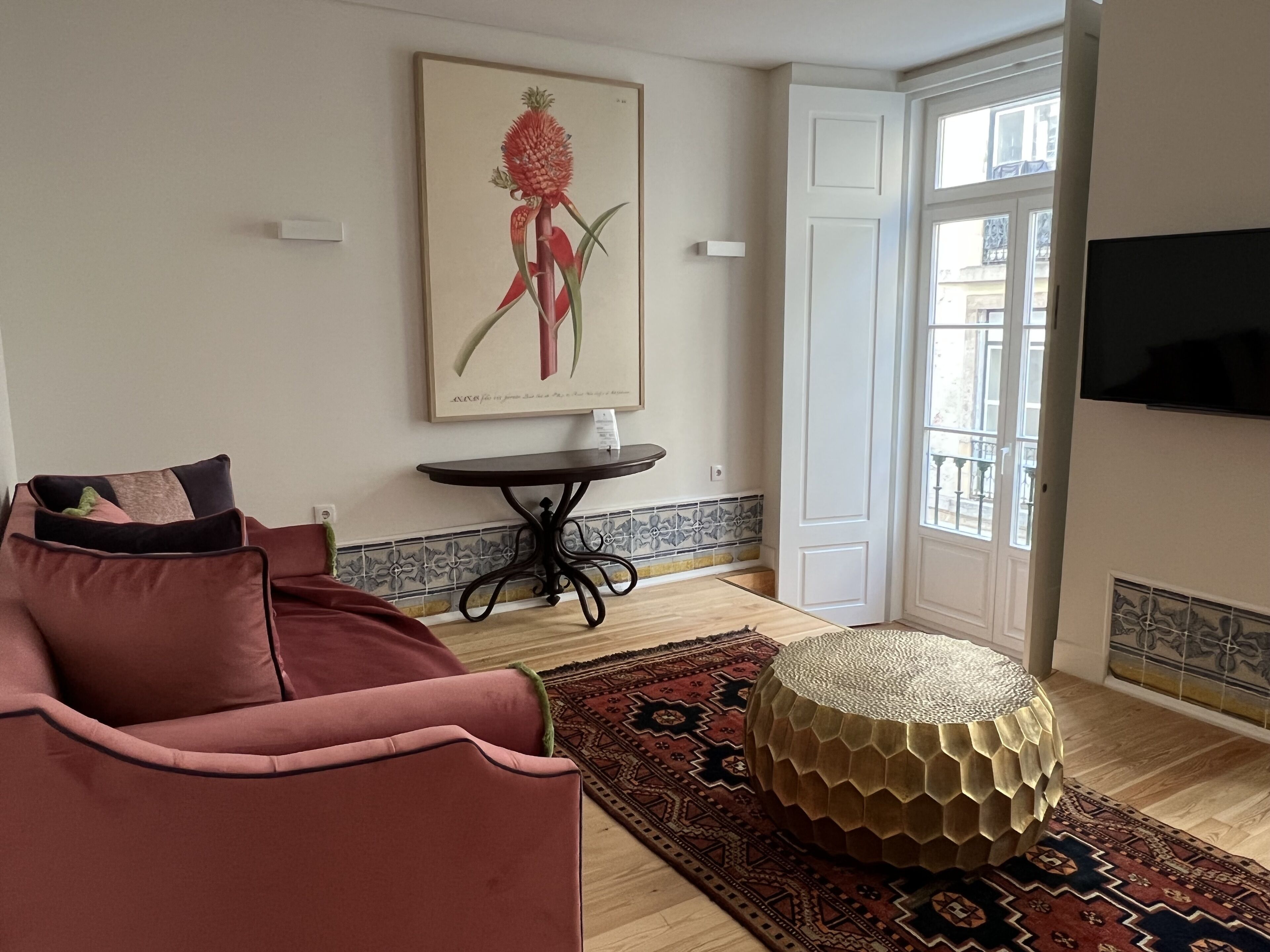 Ein Wohnzimmer mit einem roten Sofa, einem runden Hocker, einem kleinen Tisch und einem botanischen Druck im Bilderrahmen an der Wand.