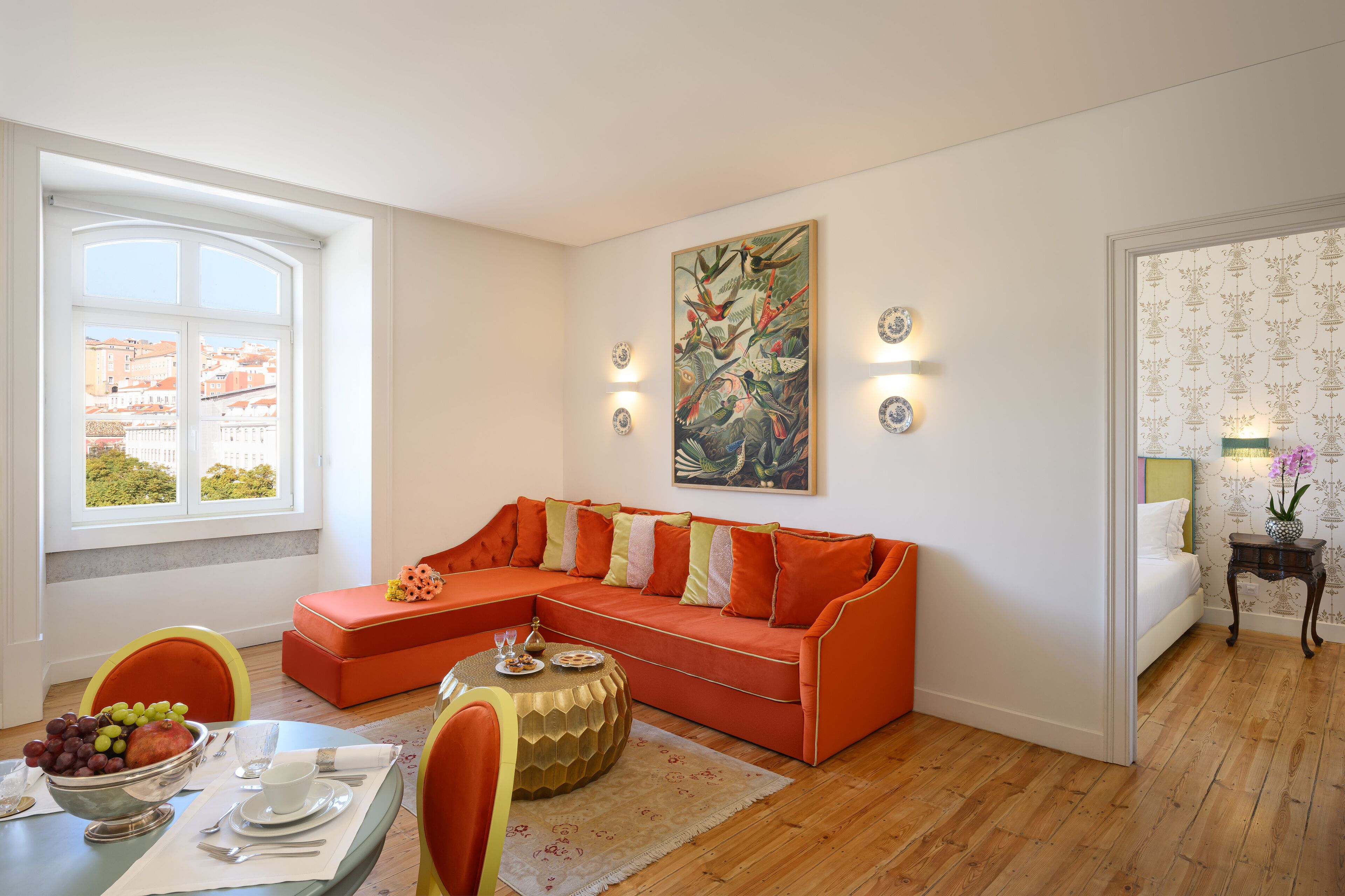 Un salon moderne avec un canapé d’angle, une table à manger avec des chaises et une grande fenêtre offrant une vue sur les bâtiments.