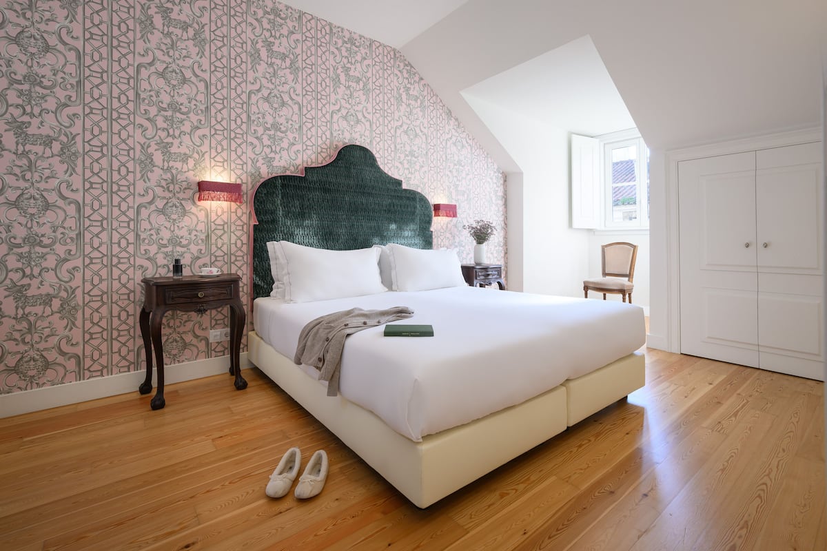 Une chambre avec un grand lit, un plancher en bois, un papier peint à motifs et une fenêtre donnant sur un beau paysage.