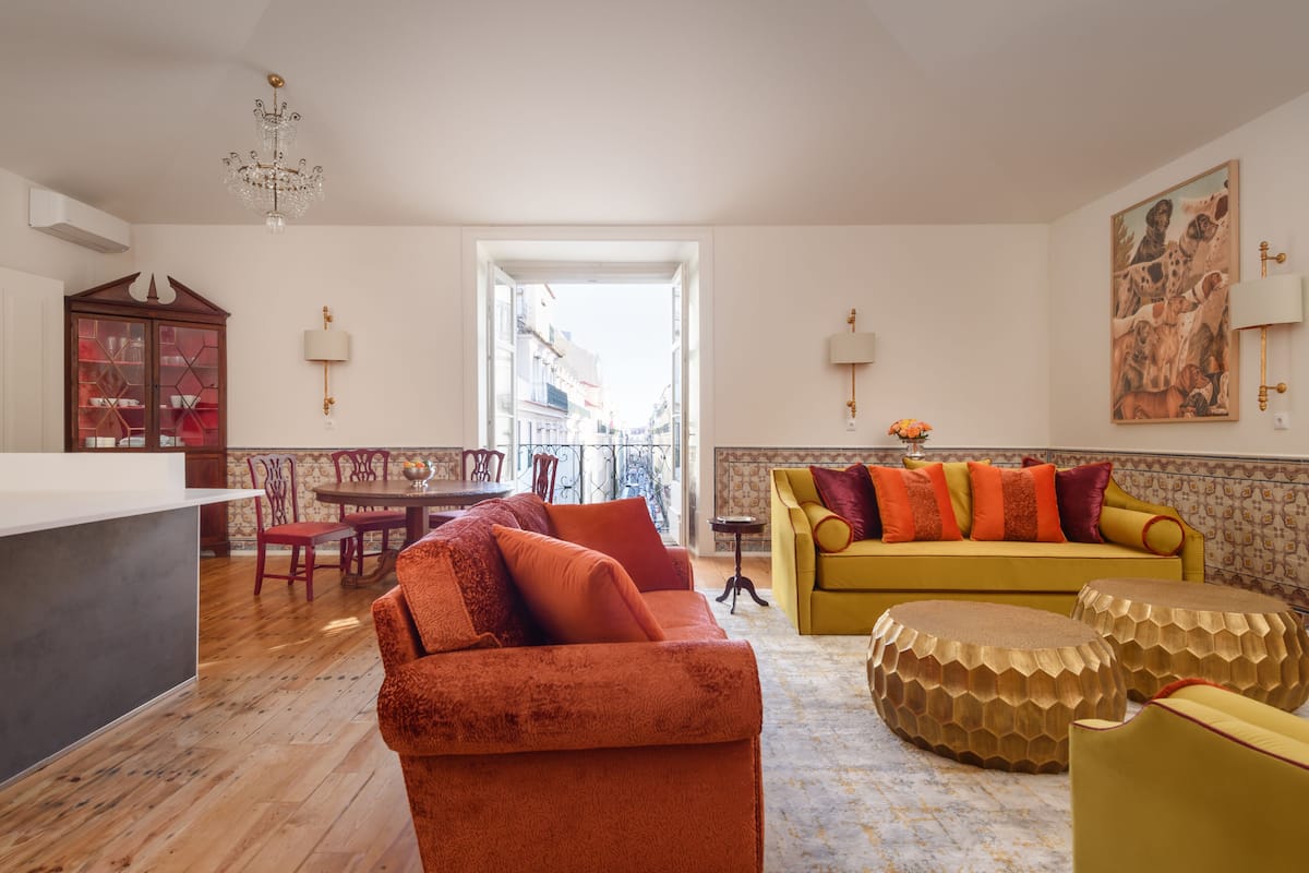 Un salon spacieux avec un canapé jaune, un fauteuil orange et un coin repas comprenant une table et des chaises en bois.