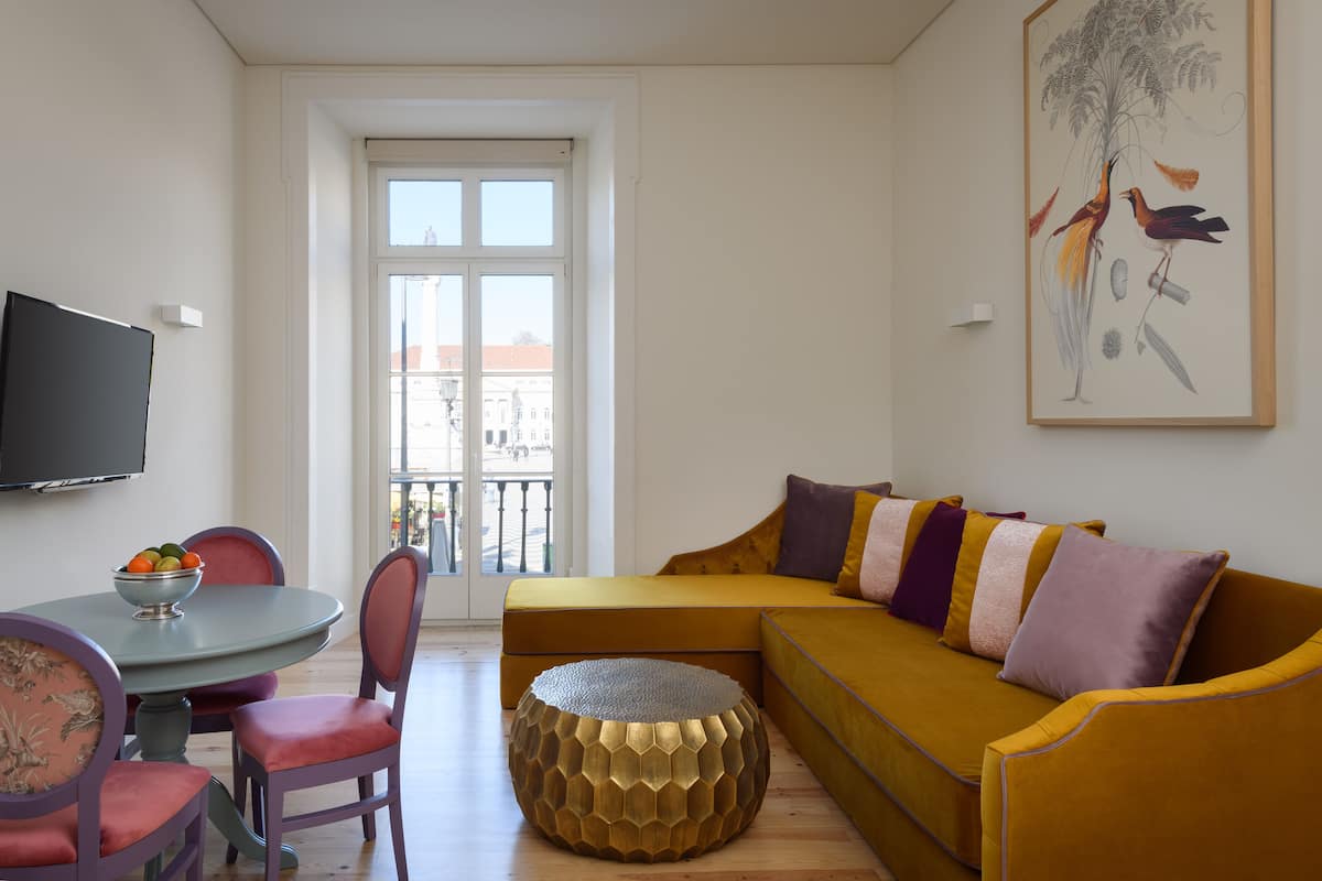 Un salon comprenant un canapé, des fauteuils, un pouf rond, une table à manger avec un saladier de fruits et un tableau accroché au mur.