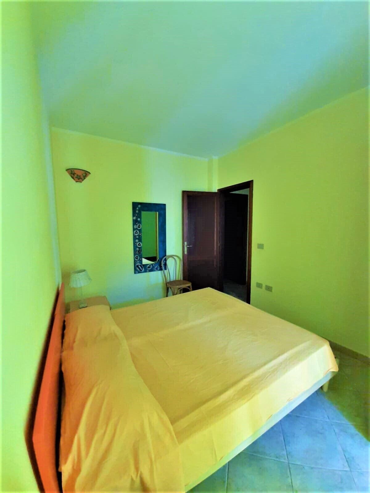 Ein Zimmer mit einem großen Bett, einem Sessel, einem kleinen Tisch und einem Spiegel an der Wand.