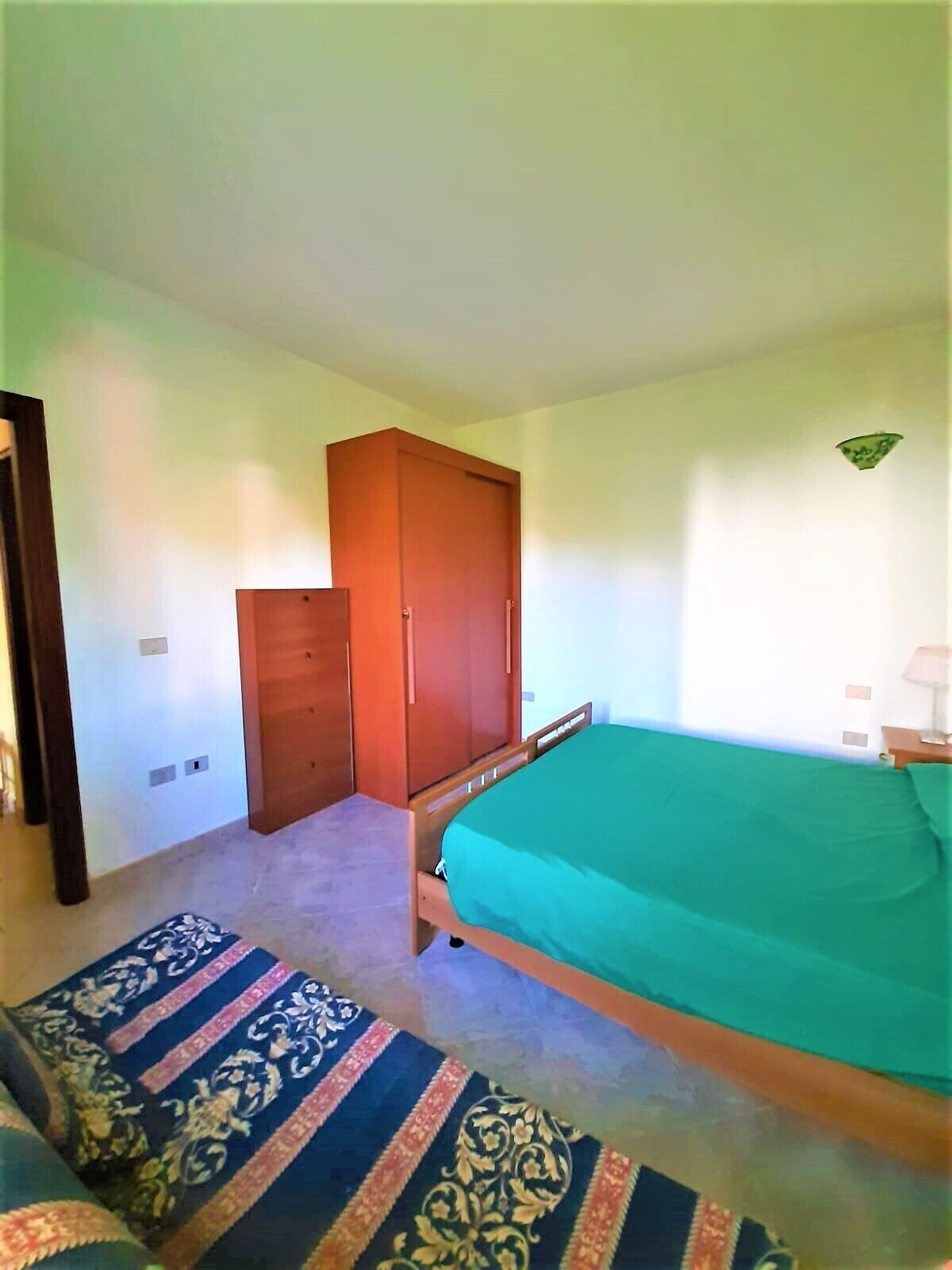 A bedroom with a bed, a wardrobe, and a patterned rug.