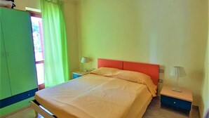 Ein Schlafzimmer mit einem Bett, einem Nachttisch, einem Sessel, einem Kleiderschrank und einem Fenster mit Vorhängen.