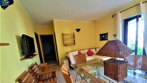 Ein Wohnzimmer mit einer Couch, Sesseln, einem Glastisch, einem Fernseher und einer Korbtischlampe.