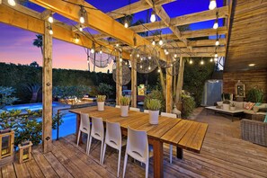 Een buiten eethoek met een houten pergola, lichtjes en potplanten.