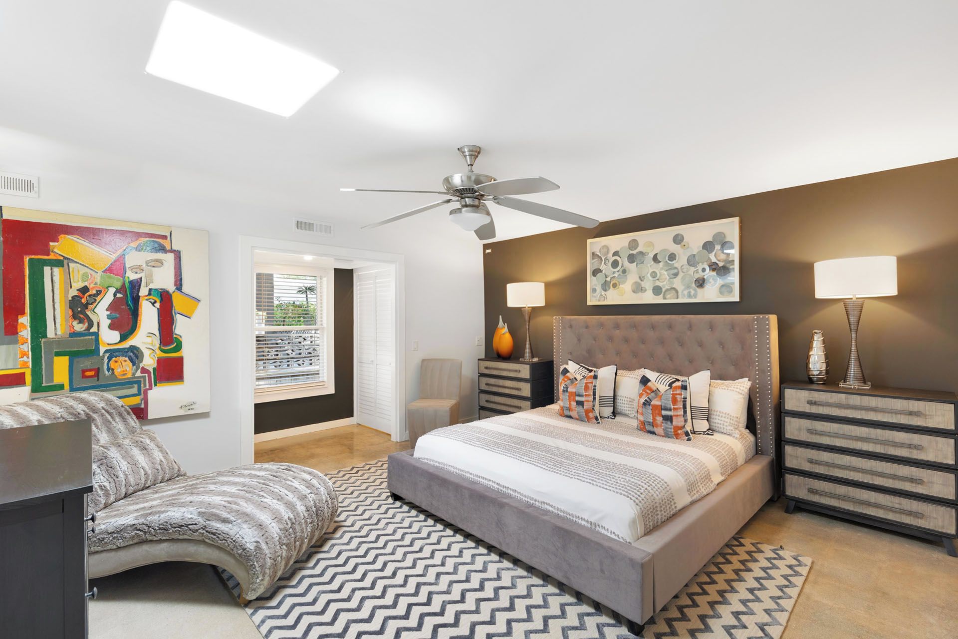 A modern bedroom with a large bed, a ceiling fan, and artwork on the walls.