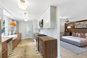 Een moderne keuken met een centraal eiland, een eethoek en een slaapkamer met een bed en een plafondventilator.