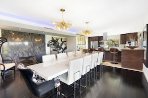 Uma cozinha moderna com painel de mármore, uma área de jantar com cadeiras brancas e um espaço bar com banquetas.